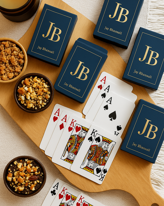 Playing cards with 'JB' branding on a wooden board with snacks and a candle.